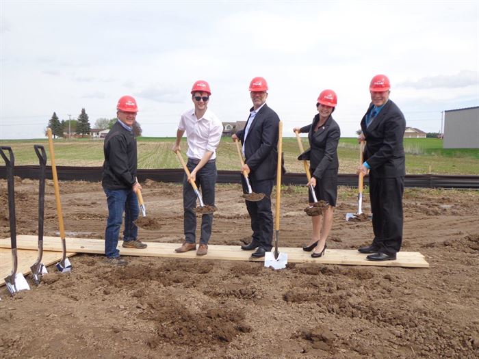 Five people in business attire with hardhats and shovels digging