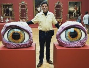 Bruce Winkler standing in gallery between two eye sculptures