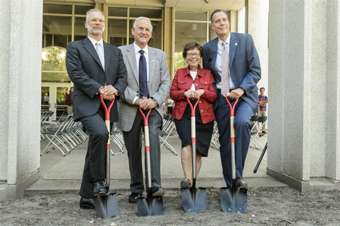 Four people stepping on shovels in front of chemistry building