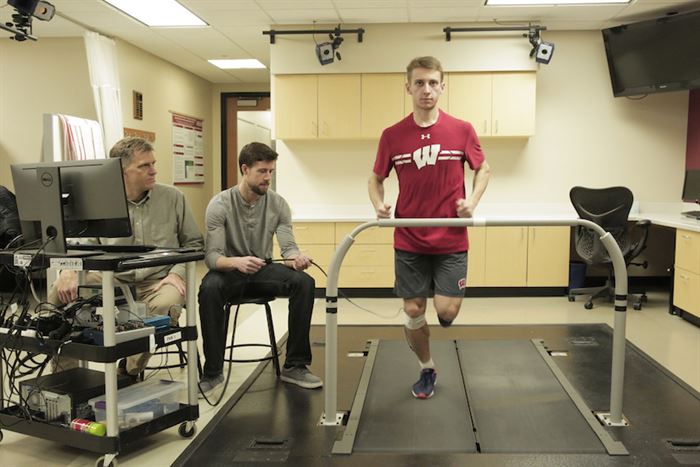 Man running on a treadmill in a lab while two men check computer and wires