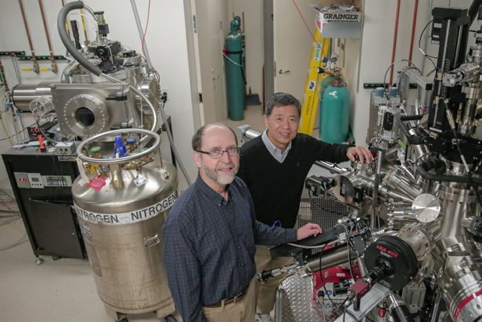 Eom and Rzchowski standing in a large room filled with complex machines