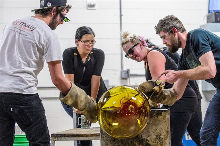 Four people creating a glass sculpture in a workshop