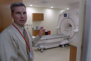 Frank Korosec gesturing to a combination MR-PET scanner