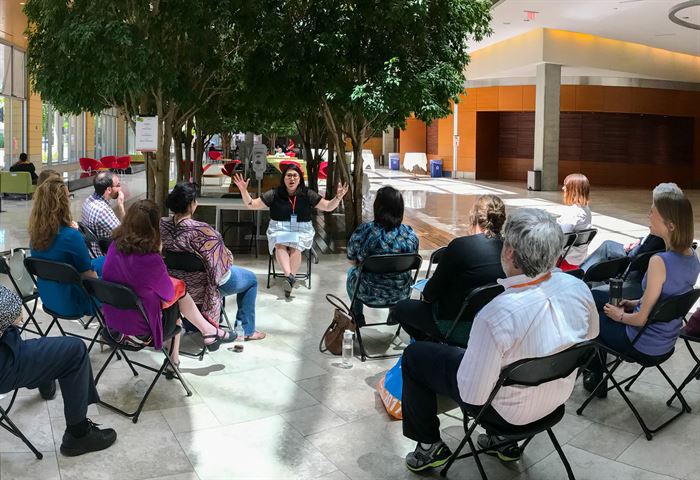 People sitting on folding chairs while a woman talks