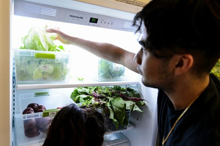 Person reaching into fridge grabbing bag of lettuce
