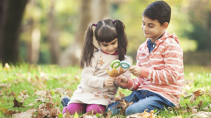 Two children sitting looking at a leaf through magnifying glasses