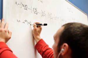 Person writing a mathmatical formula on a whiteboard