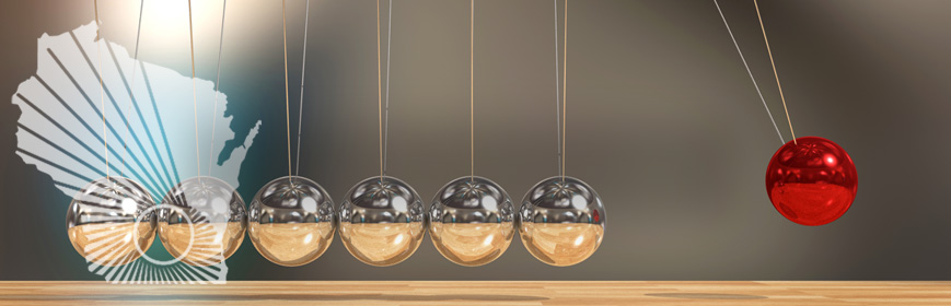 A closeup of the metal balls of a Newton's Cradle, one ball swinging upward is UW red