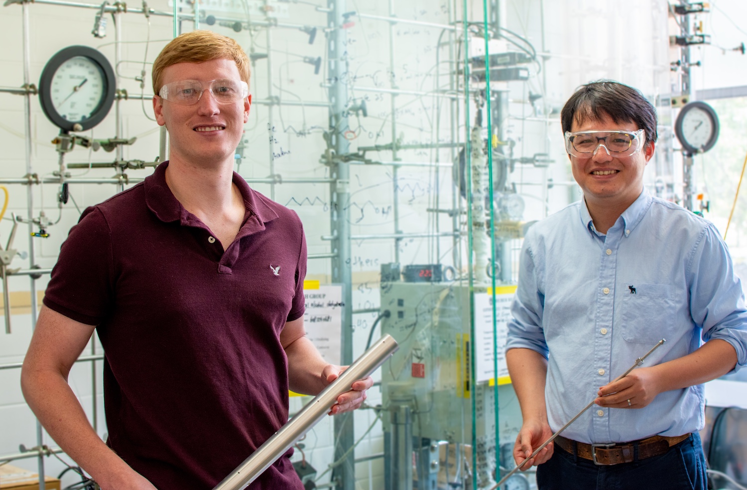 Two men in protective goggles pose in a science lab.